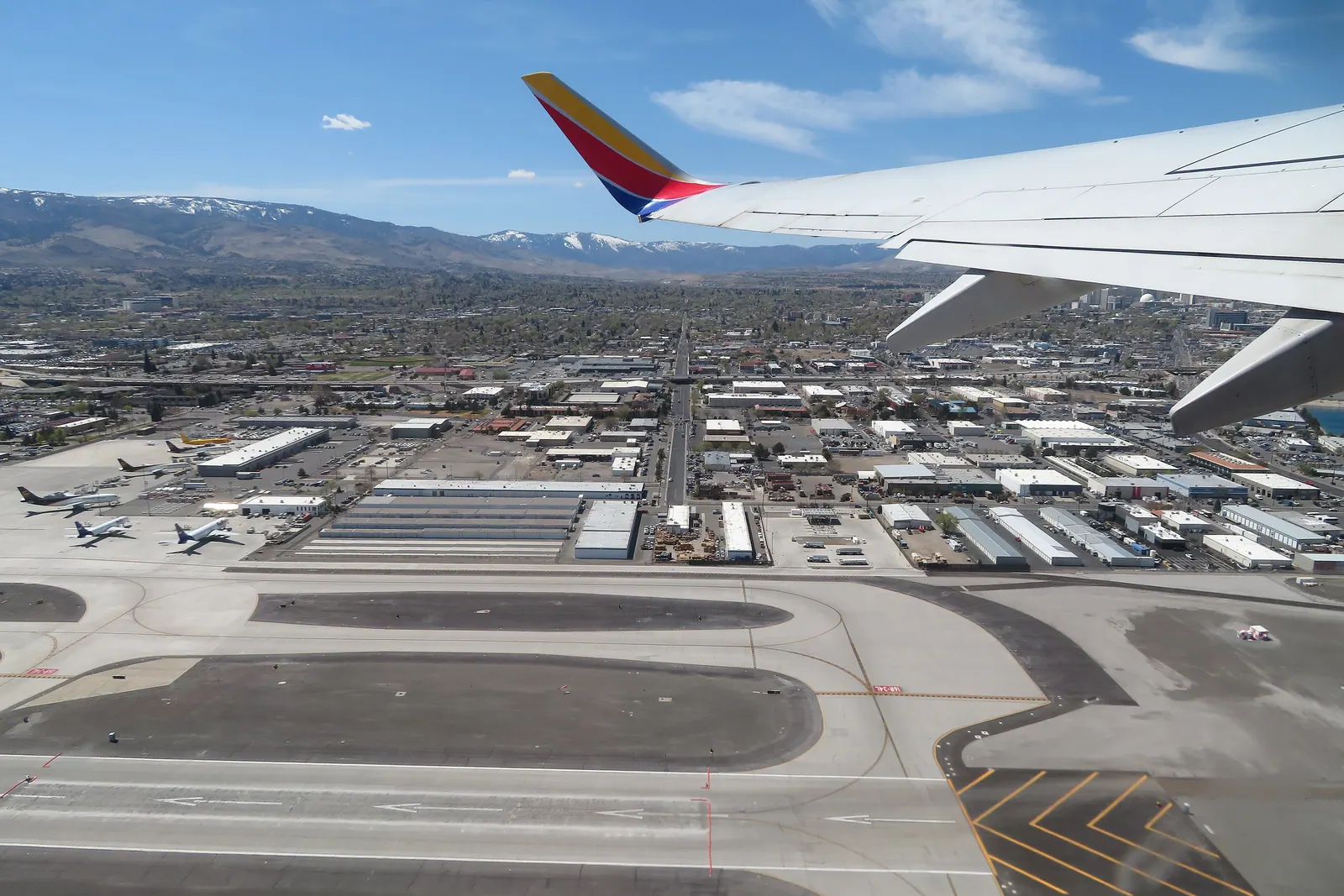 An airliner wing over the runway as a flight takes off from Reno-Tahoe International, with Reno and snowy mountains beyond