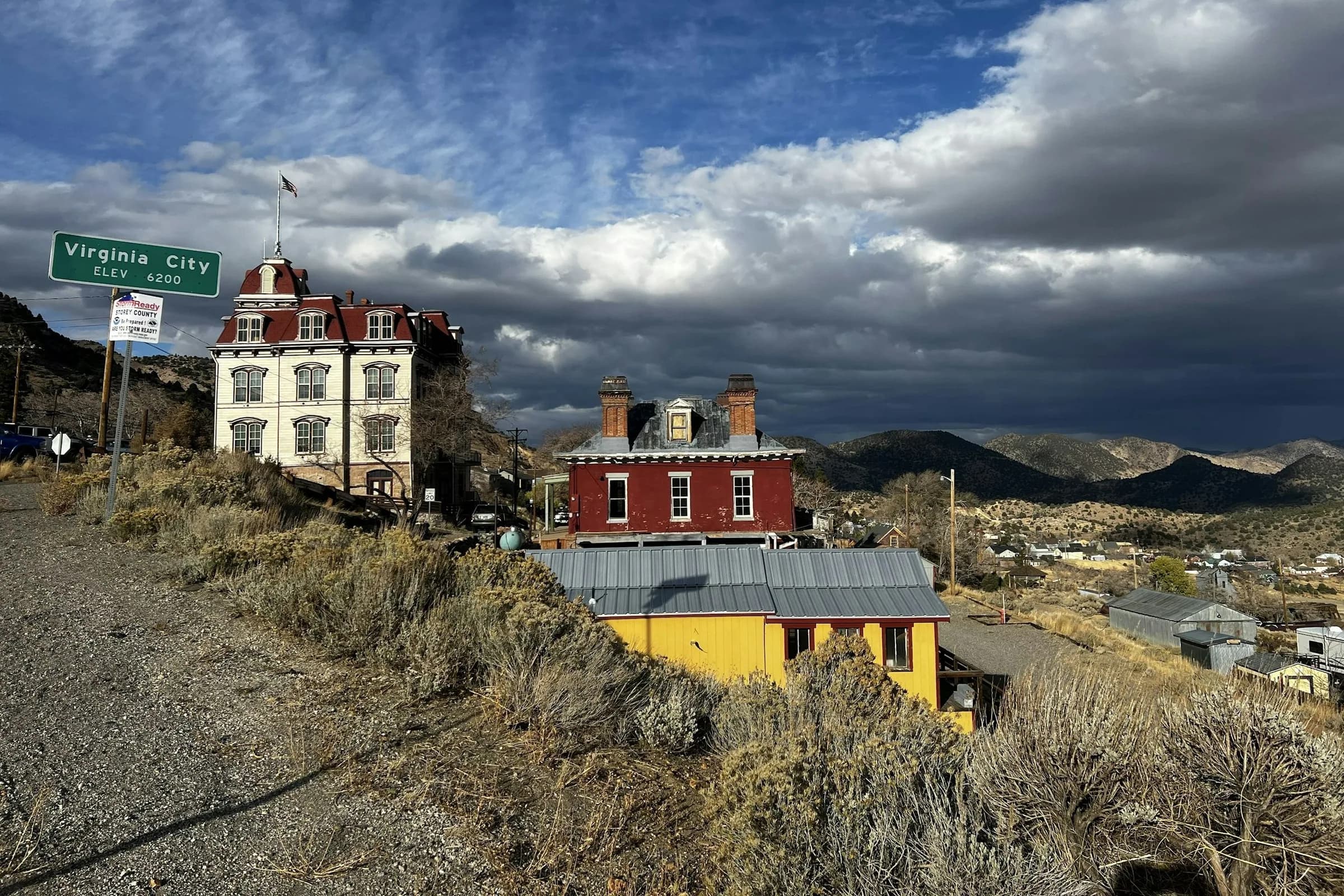 The Virginia City town sign beside historic Victorian buildings on the hillside, under a dramatic cloudy sky